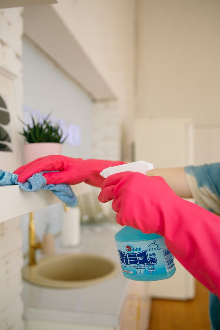 Personne utilisant un vaporisateur et un chiffon pour nettoyer une étagère de cuisine, en veillant à l'hygiène et à la propreté.